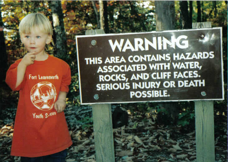 Boy stands beside a danger sign, contemplating risk